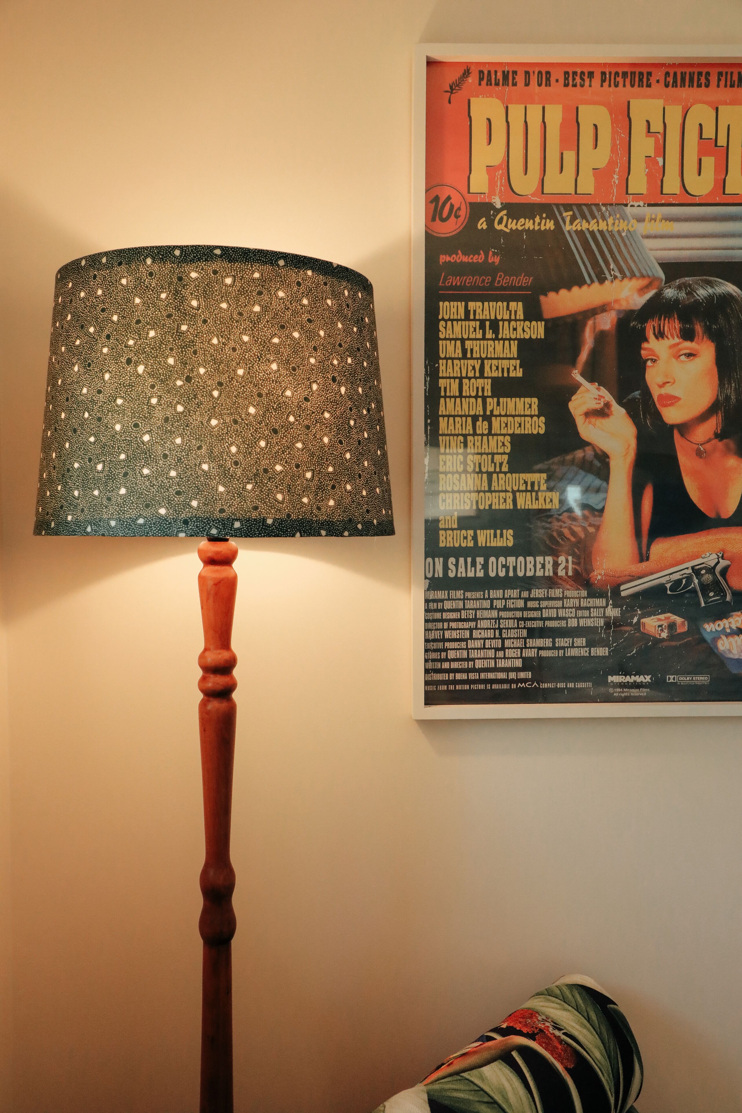 A lamp with a patterned lampshade and a movie poster on the wall.