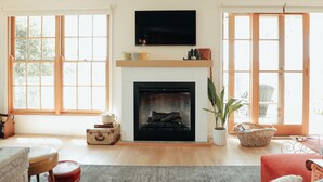 A living room with a fireplace, large windows, a television, and a cozy seating area. - Luxury Couples' Retreat Beside the Beautiful Barwon River (Highton)