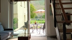 A modern living room with a sofa, coffee table, and a dining area with chairs and an umbrella. A staircase is visible to the right.