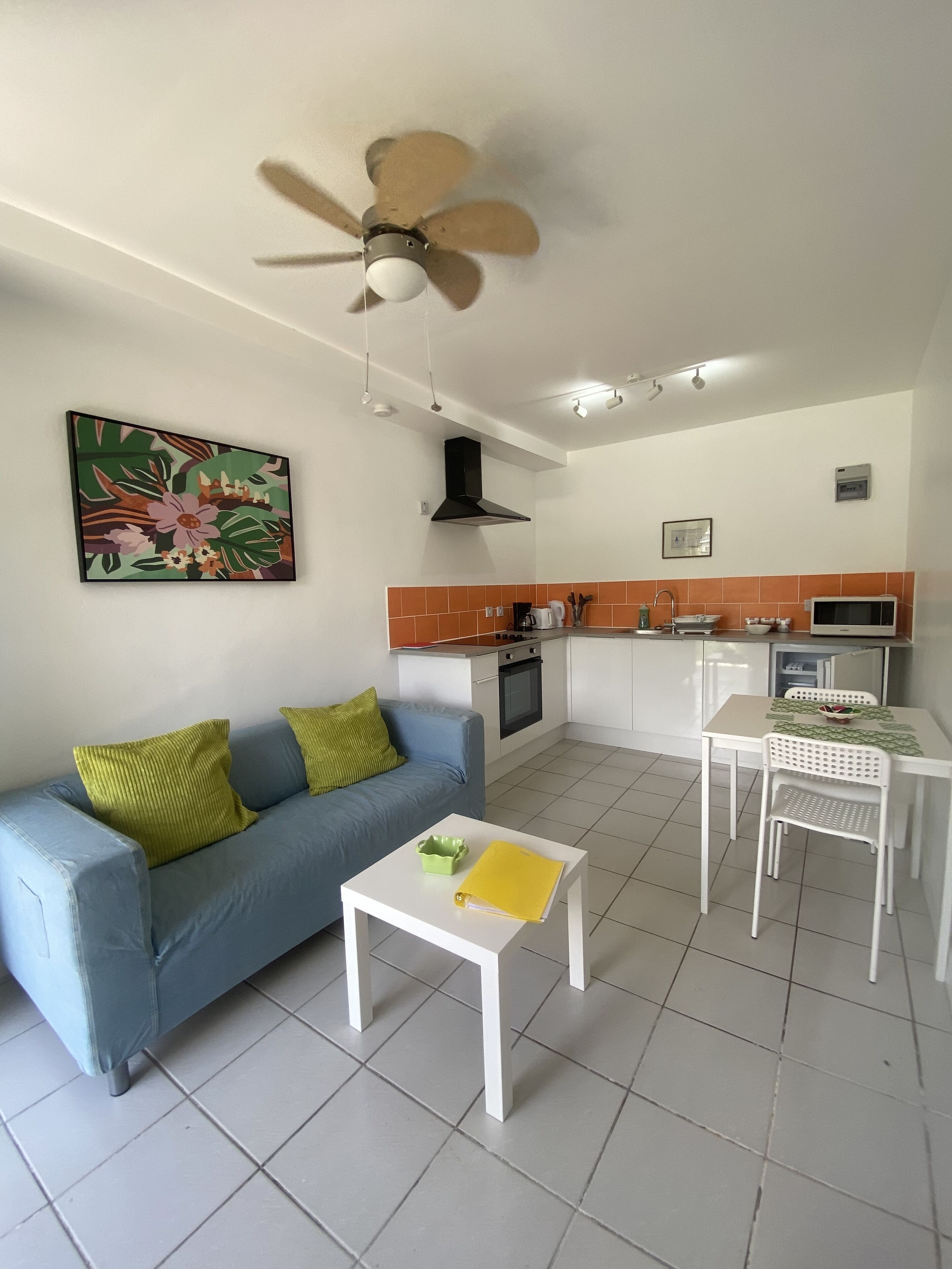 Ein Wohnzimmer mit einem blauen Sofa, einem weißen Couchtisch und einem Deckenventilator.