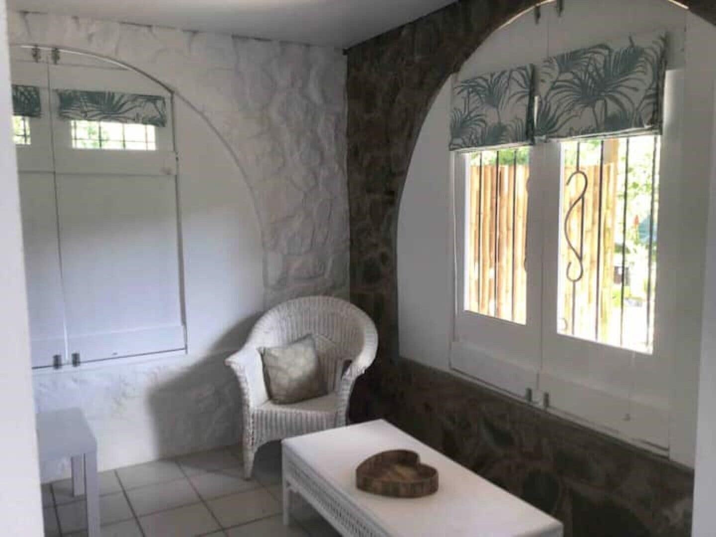 Une salle de bain avec un mur en pierre, une chaise blanche, une petite table et une fenêtre donnant sur un paysage verdoyant.