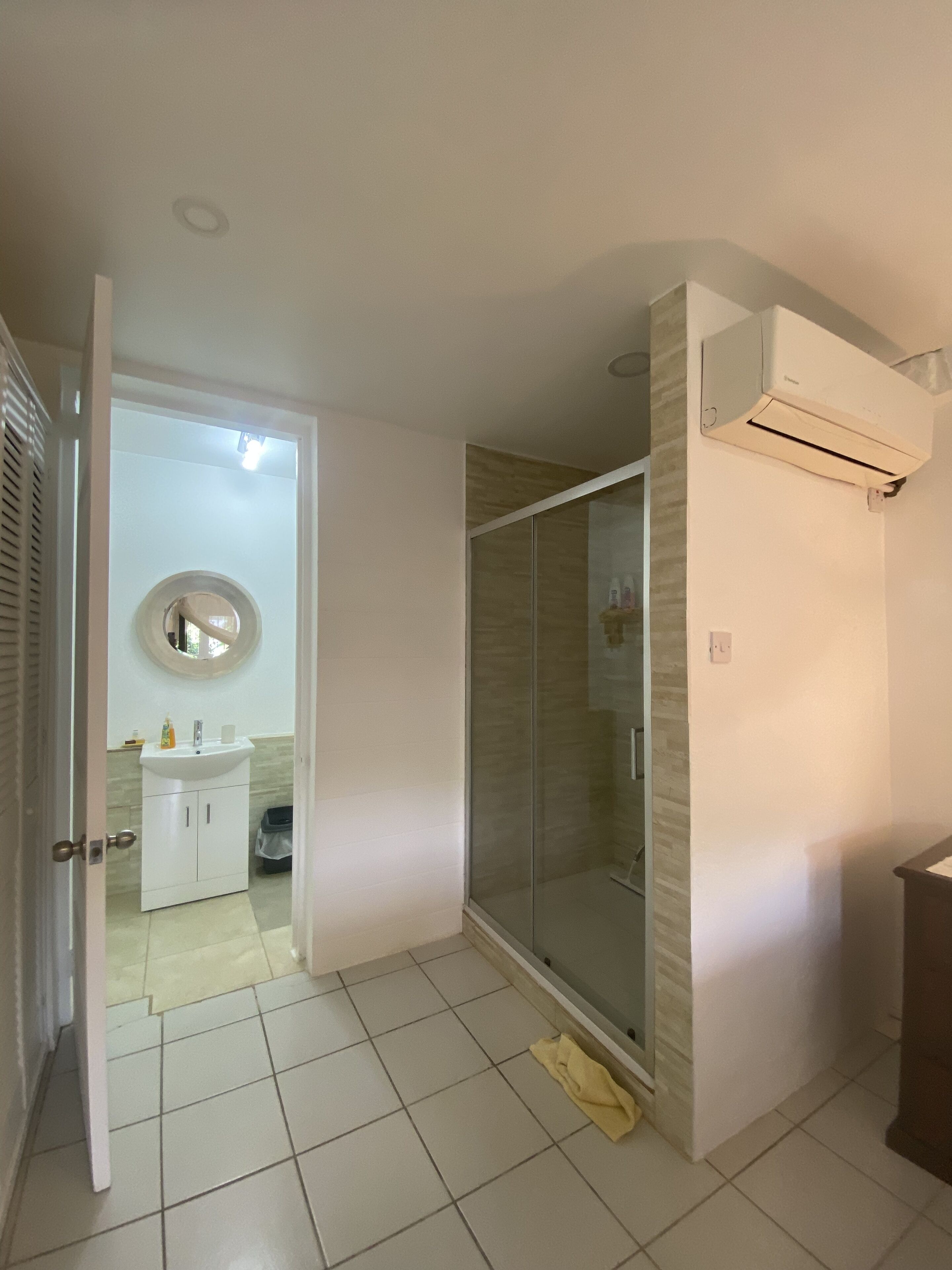 Een badkamer met een douchecabine van glas, een wit wastafelmeubel en een spiegel.