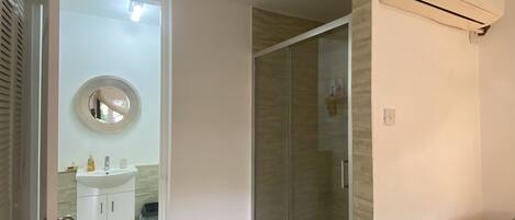A bathroom with a glass shower enclosure, a white sink, and a mirror.
