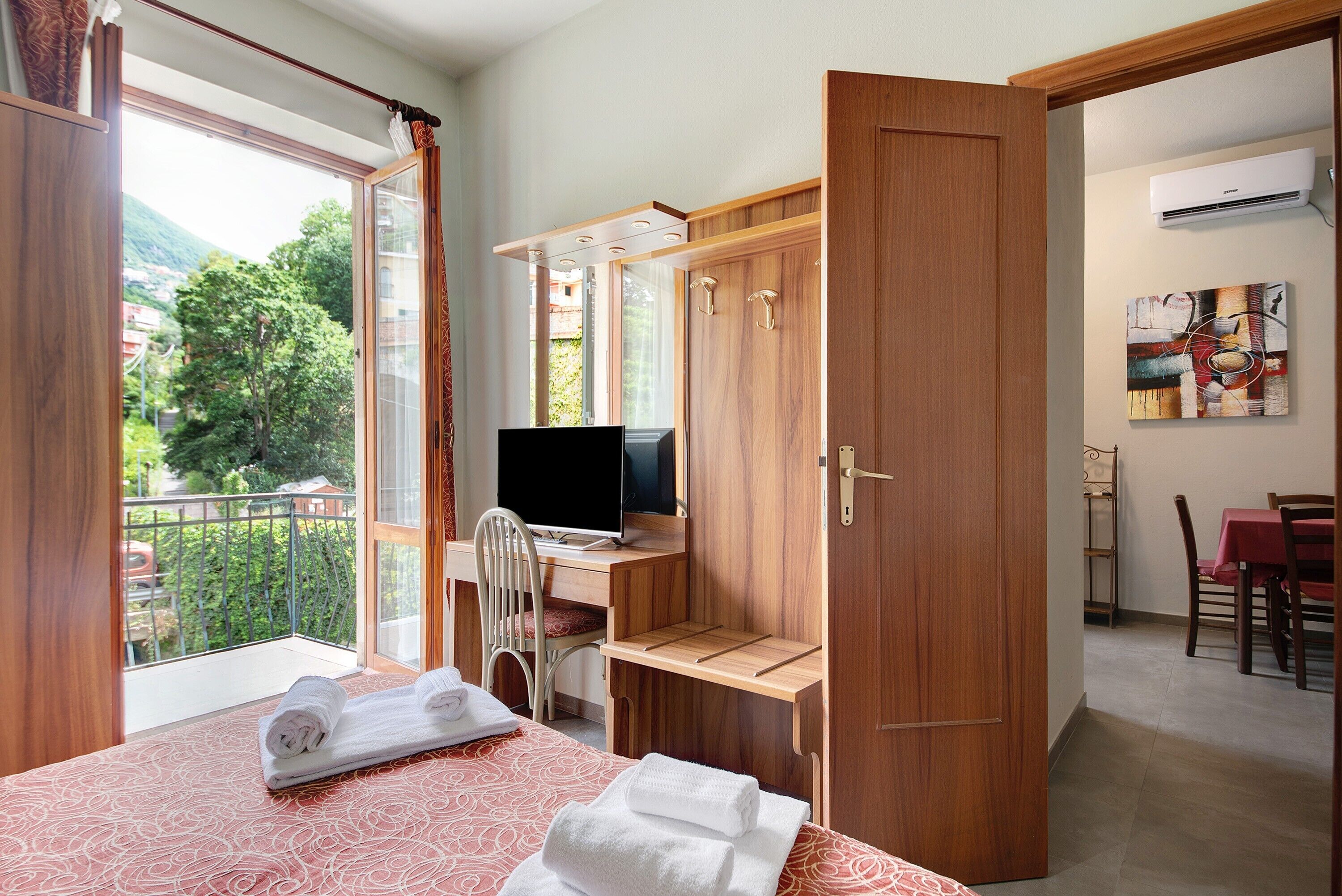 Ein Hotelzimmer mit einem Bett, einem Schreibtisch mit Computer, einem Stuhl, einem Essbereich und Blick auf Grünflächen.