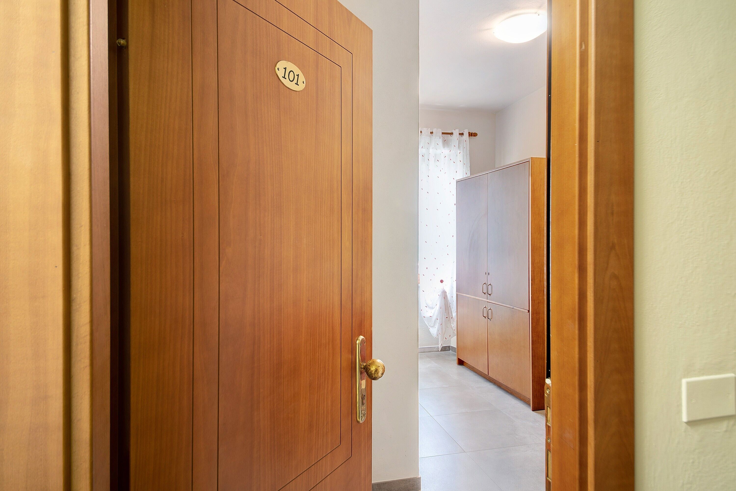 A wooden door with a brass handle and a number plate, leading to a room with a tiled floor and a curtain.