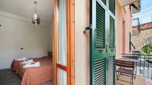 Une chambre d’hôtel avec deux lits, un balcon doté d’une table et de chaises, et un luminaire suspendu.