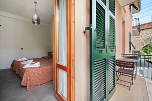 Habitación de hotel con dos camas, un balcón con mesa y sillas, y una lámpara colgante.