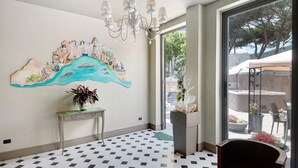 Une chambre d’hôtel dotée d’une grande fenêtre, d’un lustre, d’une fresque murale, d’une plante en pot et d’un sol à carreaux.