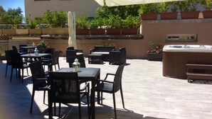 Eine Terrasse im Freien mit Tischen, Stühlen, einem Whirlpool und Blumentöpfen.