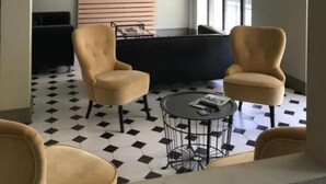 Ein modernes Wohnzimmer mit einem Kronleuchter, zwei Sesseln, einem runden Couchtisch, einem Flachbildfernseher, der an einer Holzvertäfelung angebracht ist, und einem großen Fenster.