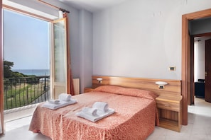 Une chambre à coucher comprenant un lit, une table de chevet, une commode, une fenêtre donnant sur un paysage agréable et une porte.