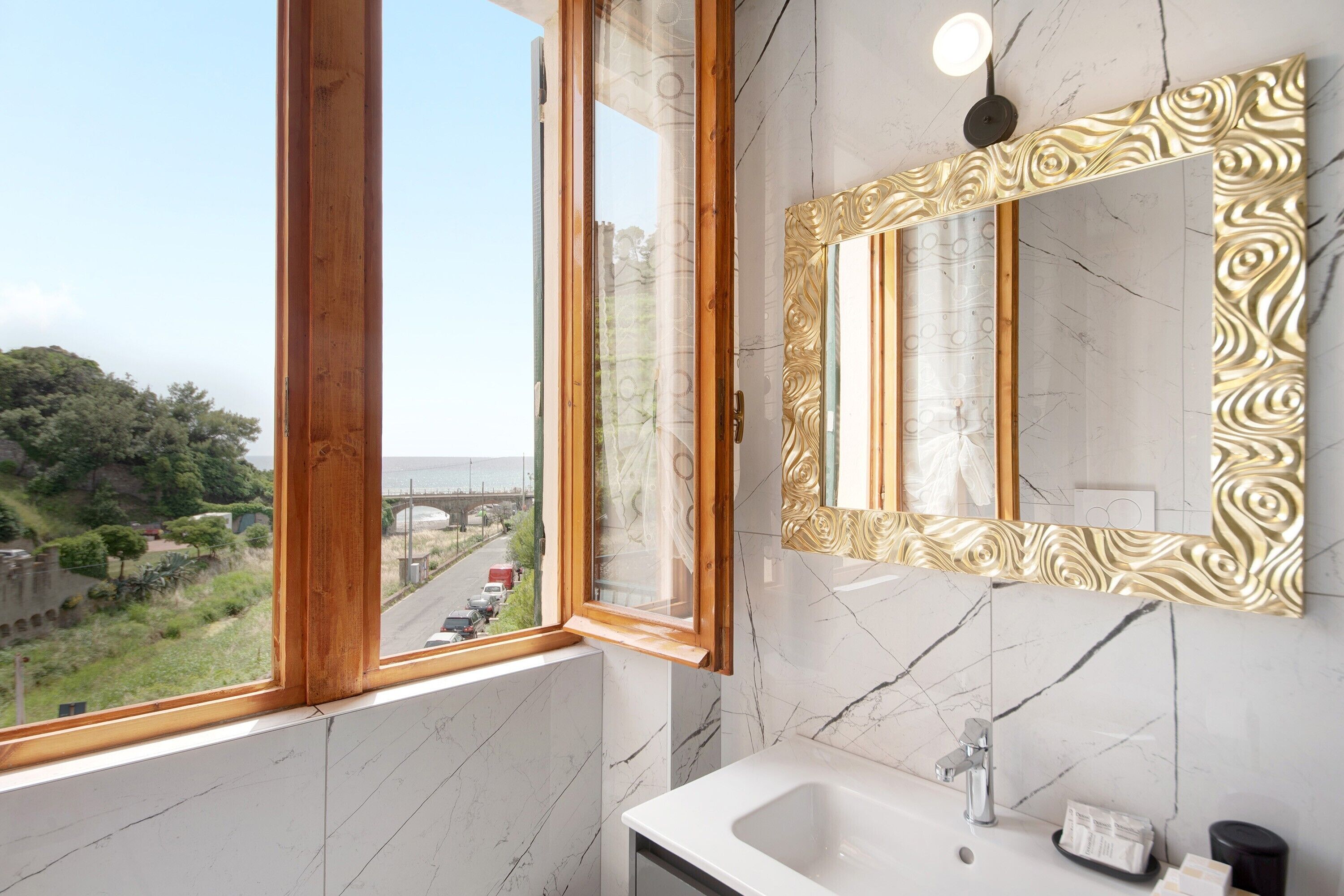 Ein Badezimmer mit großem Fenster, Marmorwaschbecken und spiegel mit goldener Rahmung.