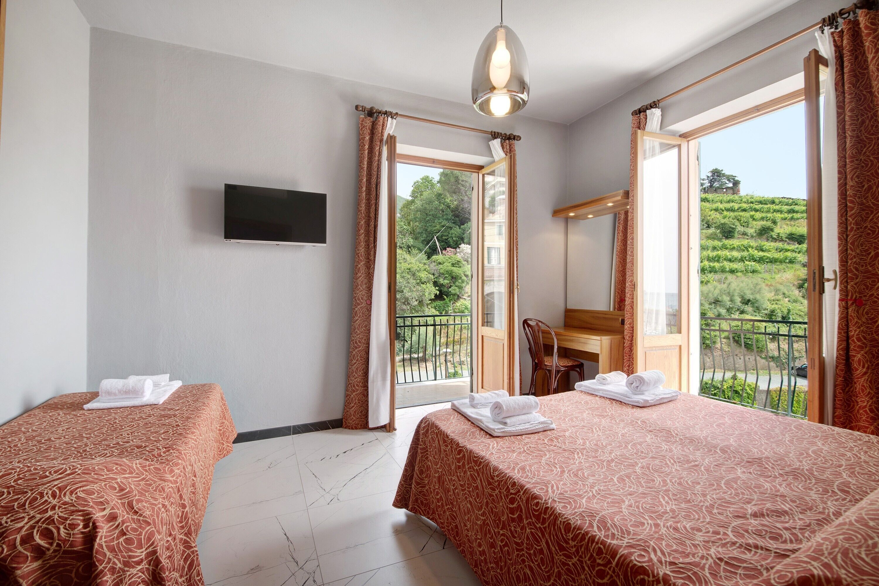 Hotelkamer met twee bedden, een televisie, een bureau en een balkon met uitzicht op groen.