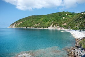 Kustlandschap met helder turquoise water, een rotsachtige kustlijn en een heuvel met schaarse begroeiing.