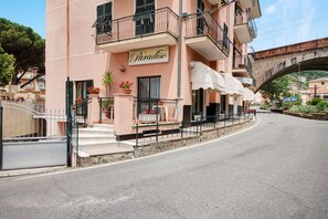 Un hôtel appelé « Paradiso », doté d’un balcon, de sièges en plein air et d’un pont de pierre en arrière-plan.