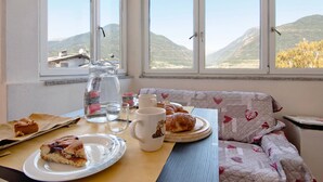 Mesa de pequeno-almoço com pastelaria, um copo de água e uma chávena, com vista para montanhas através da janela.