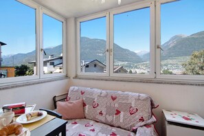 Een kamer met een bank, een tafel met eten erop en een raam met uitzicht op een berg.