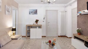 Uma sala de estar com sofá, mesa de centro com flores, televisão em um móvel, porta e radiador.