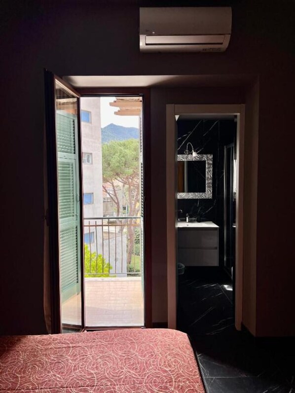 A hotel room with a bed, an open door leading to a balcony, and a bathroom with a mirror and sink.