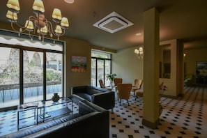 A hotel lobby with a checkered floor, a sofa, chairs, a painting, and a large window with a view.