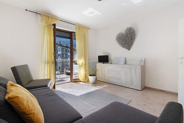 A modern living room with a sofa, a chair, a TV, a cabinet, and a heart-shaped wall decoration.