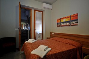 A hotel room with a bed, a mirror, a door, and a wall with three paintings.