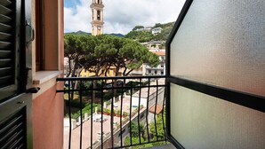 A balcony with a view of a clock tower, trees, and residential buildings.