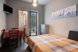 Une chambre à coucher avec un lit, une table à manger avec des chaises, un téléviseur et un tableau représentant des voiliers accroché au mur.