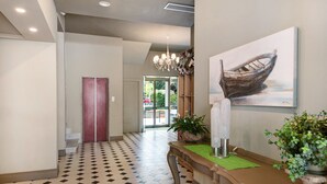 A hotel lobby with a checkered floor, a reception desk, a painting of a boat, and a staircase.