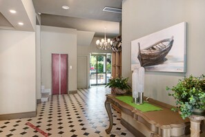 Un hall d’hôtel avec un sol à carreaux, un comptoir d’accueil, un tableau représentant un bateau et un escalier.