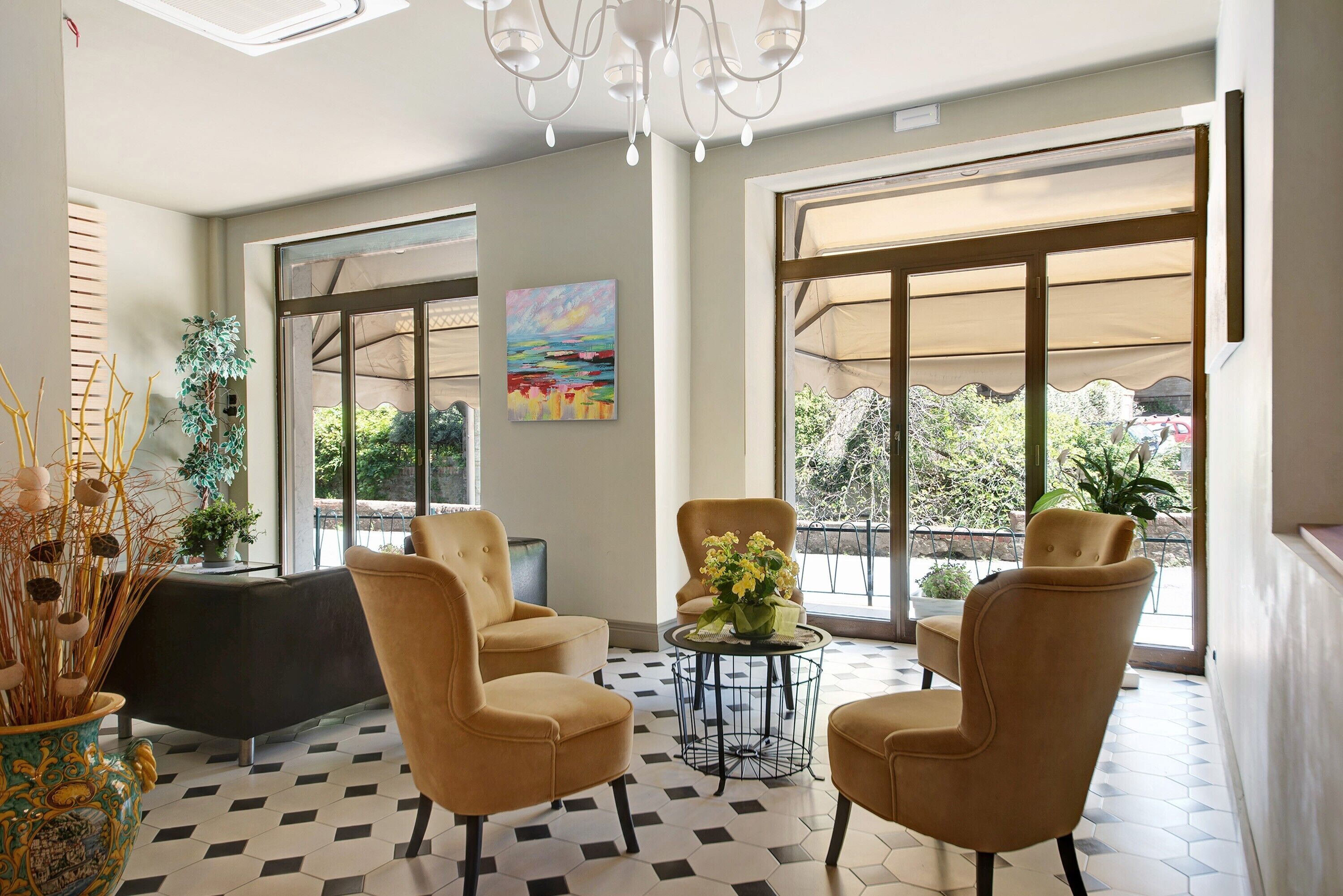 A lobby with a checkered floor, two sofas, a table with flowers, a painting, and large windows with blinds.