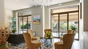 A lobby with a checkered floor, two sofas, a table with flowers, a painting, and large windows with blinds.