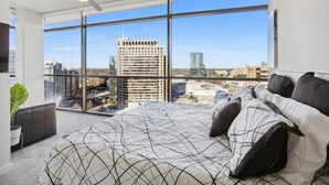 A modern bedroom with a large bed, a ceiling fan, and a city view through floor-to-ceiling windows. - The Heart of the city (Atlanta)