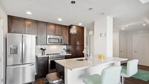 A modern kitchen with stainless steel appliances, dark wooden cabinets, and a central island with bar stools. - The Heart of the city (Atlanta)