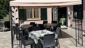 An outdoor patio with a table and chairs, a covered area, and a building in the background. - Holiday Apartment "Residence Paradiso Monolocale 305" with Balcony, A/C & Wi-Fi (Moneglia)
