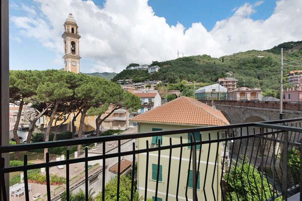 A balcony with a view of a town, including a clock tower, residential buildings, and greenery.