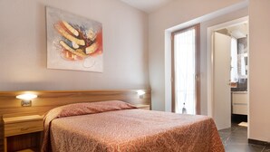 A hotel room with a bed, bedside lamps, a painting on the wall, and a bathroom visible through an open door. - Apartment 'Residence Paradiso Bilocale 304' with Balcony, Wi-Fi and Air Conditioning (Moneglia)