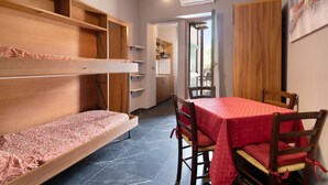 A compact room with bunk beds, a dining table with chairs, and a view of the outside. - Apartment 'Residence Paradiso Bilocale 304' with Balcony, Wi-Fi and Air Conditioning (Moneglia)