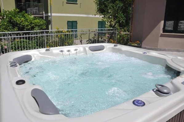Un bain à remous avec jets, entouré d’une clôture métallique, avec un bâtiment et de la verdure en arrière-plan.