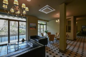 A hotel lobby with a checkered floor, a sofa, chairs, a painting, and a large window with a view.
