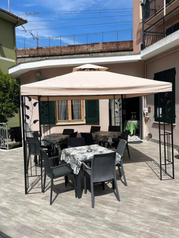 An outdoor patio with a table and chairs, a covered area, and a building in the background.