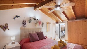 A bedroom with a bed, pillows, a bedside table with a lamp, a ceiling fan, and a wall with dreamcatchers. - Holiday Home 'Ana Townhouse' with Private Terrace, Wi-Fi and Air Conditioning (Tavira)