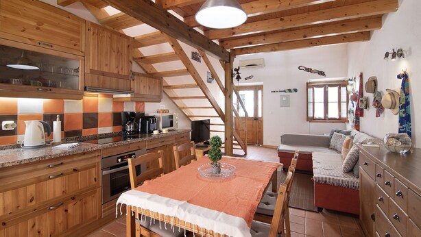 A rustic kitchen with wooden cabinets, a dining table with a white tablecloth, and a staircase leading to a loft area. - Holiday Home 'Ana Townhouse' with Private Terrace, Wi-Fi and Air Conditioning (Tavira)