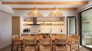 Une cuisine moderne avec des poutres en bois, une table à manger entourée de chaises en osier et une grande fenêtre donnant sur la mer.