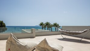 Un hamac sur un balcon donnant sur la mer, agrémenté de coussins à motifs et offrant une vue dégagée sur l’océan.