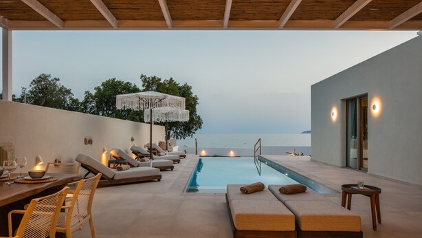 Un espace aménagé au bord de la piscine, avec des chaises longues et une table à manger, offrant une vue sur la mer.