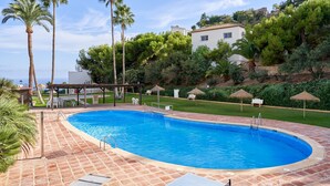 Una piscina con cubierta de baldosas, rodeada de palmeras y un césped con sillones de descanso.