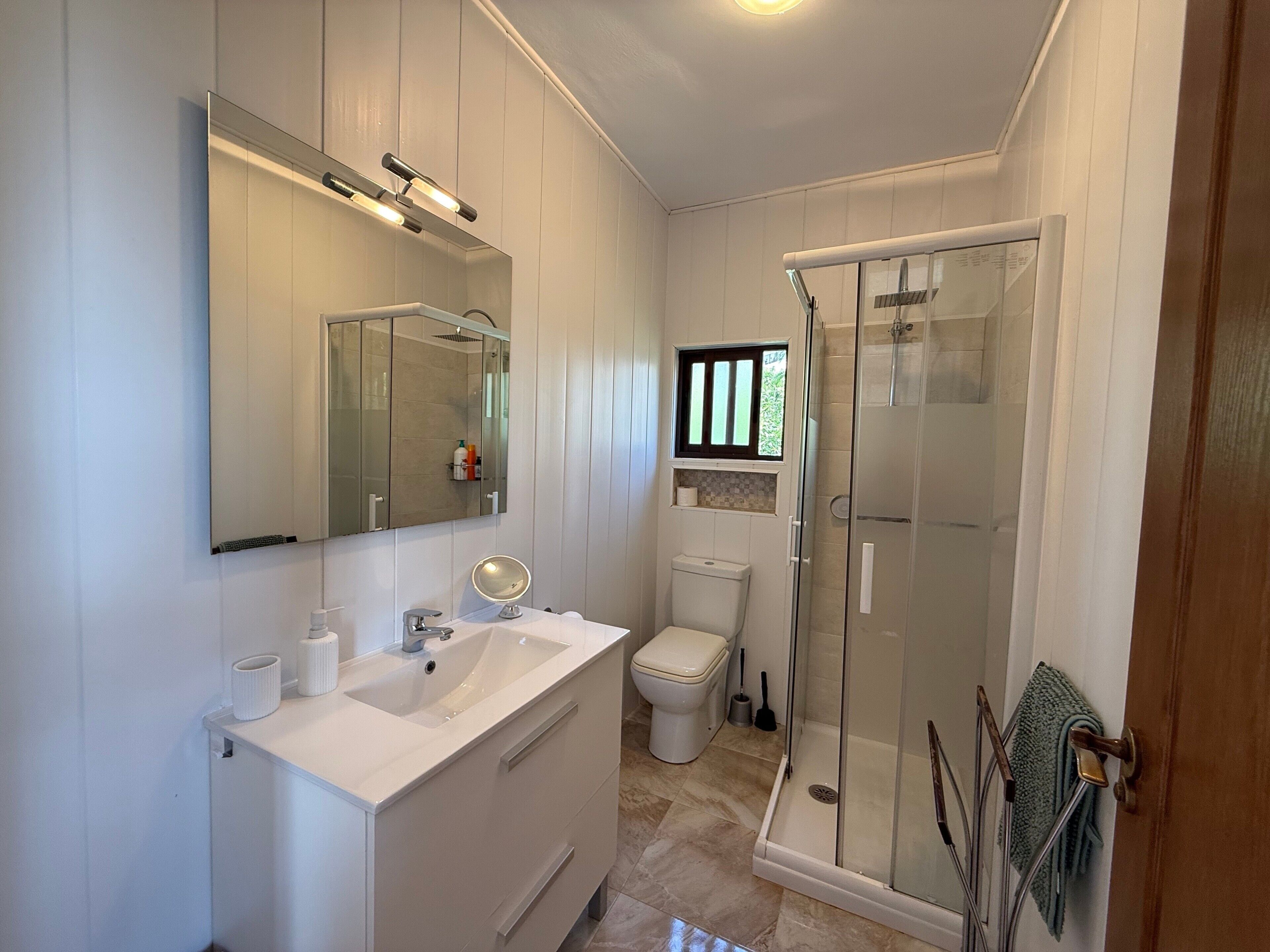 A modern bathroom with a large mirror, a sink, a toilet, and a glass-enclosed shower.