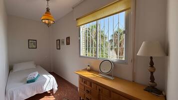 Un dormitorio con una cama, un escritorio con lámpara, una ventana con persianas y un ventilador de techo.
