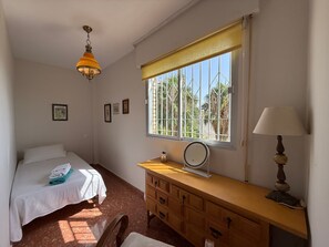 Un dormitorio con una cama, un escritorio con lámpara, una ventana con persianas y un ventilador de techo.